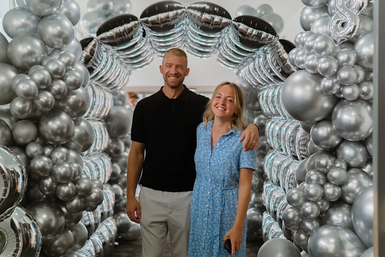 Two guests photographed in front of a full height silver chrome balloon wall