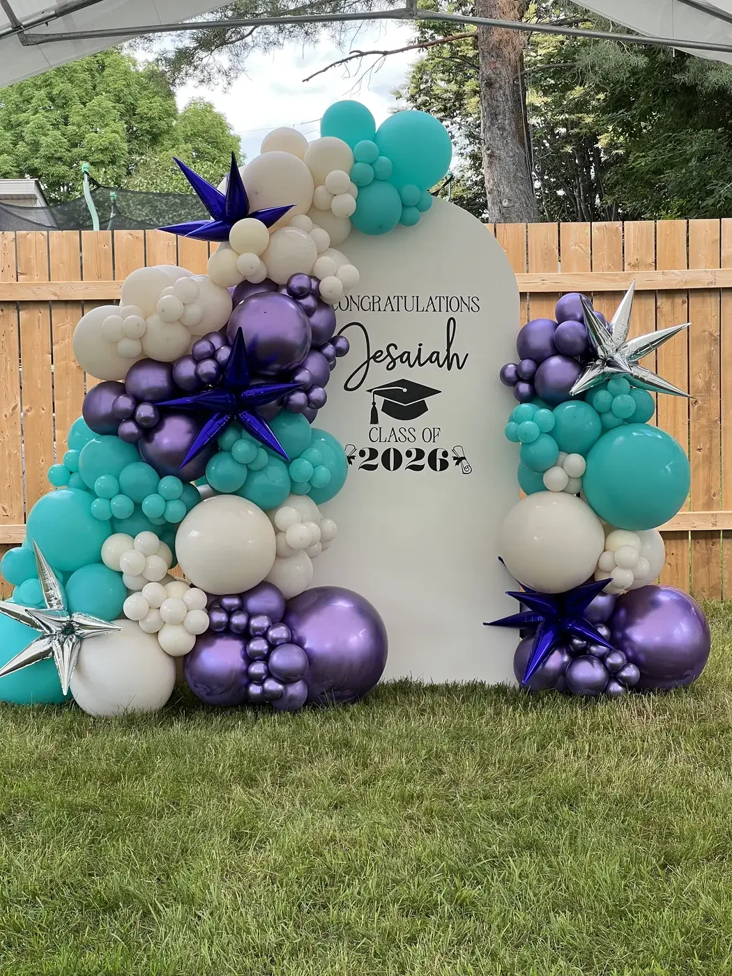 Custom painted arch backdrop with personalised vinyl lettering and a teal, purple and cream garland with star bursts