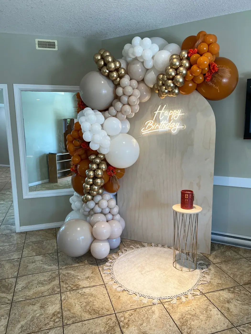 Wood grain arch with a cream, rust and copper garland and a neon birthday sign